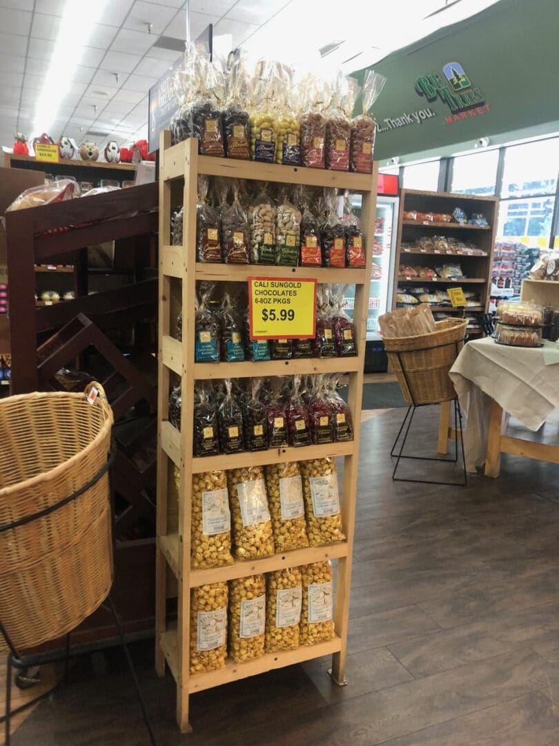 A wooden display rack filled with various packaged nuts and dried fruits, priced at $5.99, in a grocery store.