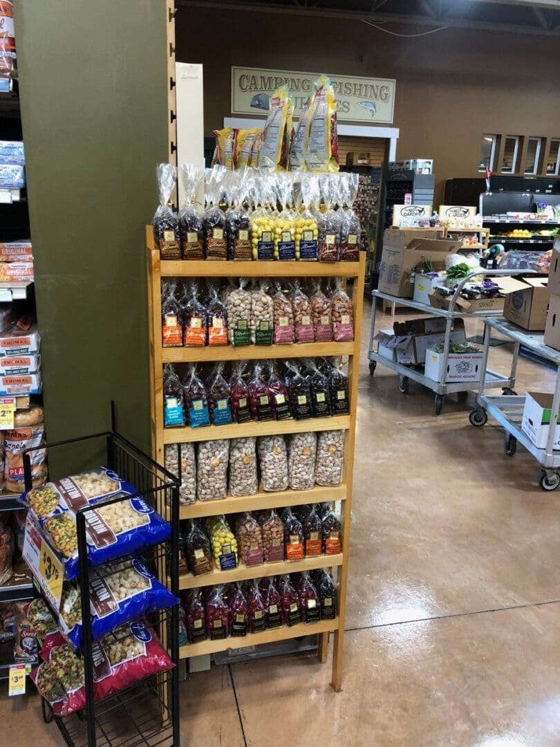 A display rack filled with various packaged snacks in a grocery store aisle, with signs for camping and fishing visible in the background.