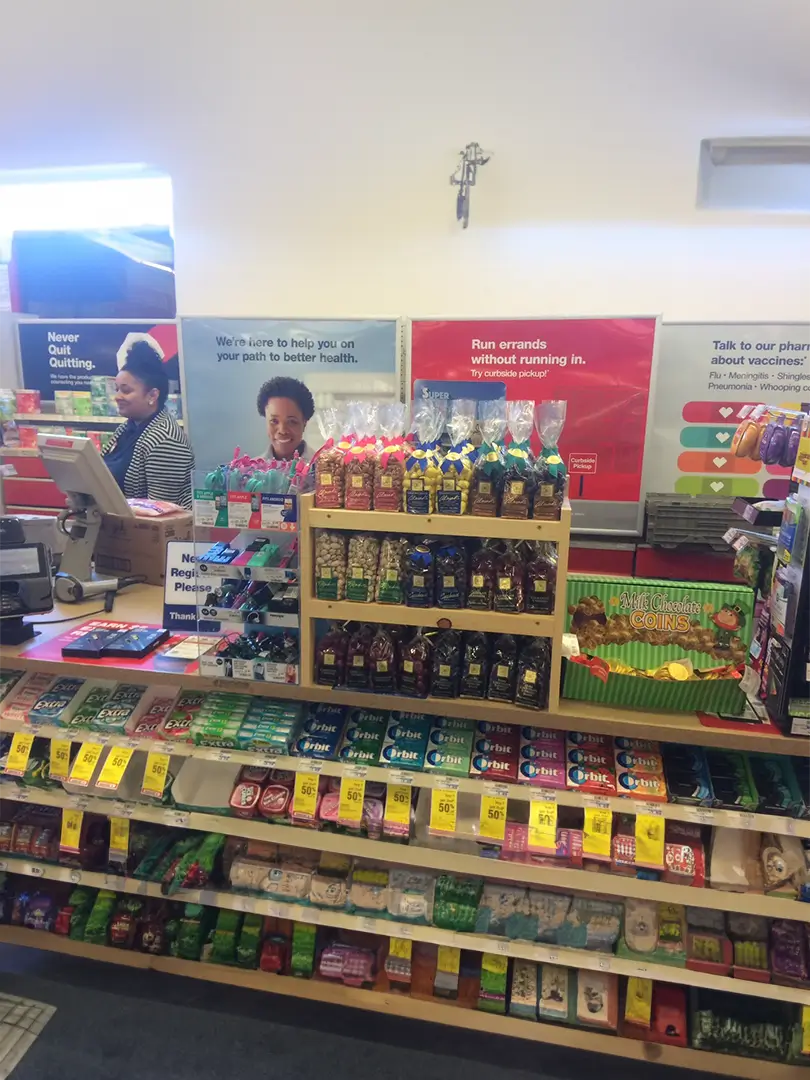 Checkout counter at a pharmacy with two clerks, stocked with various snacks and health brochures.